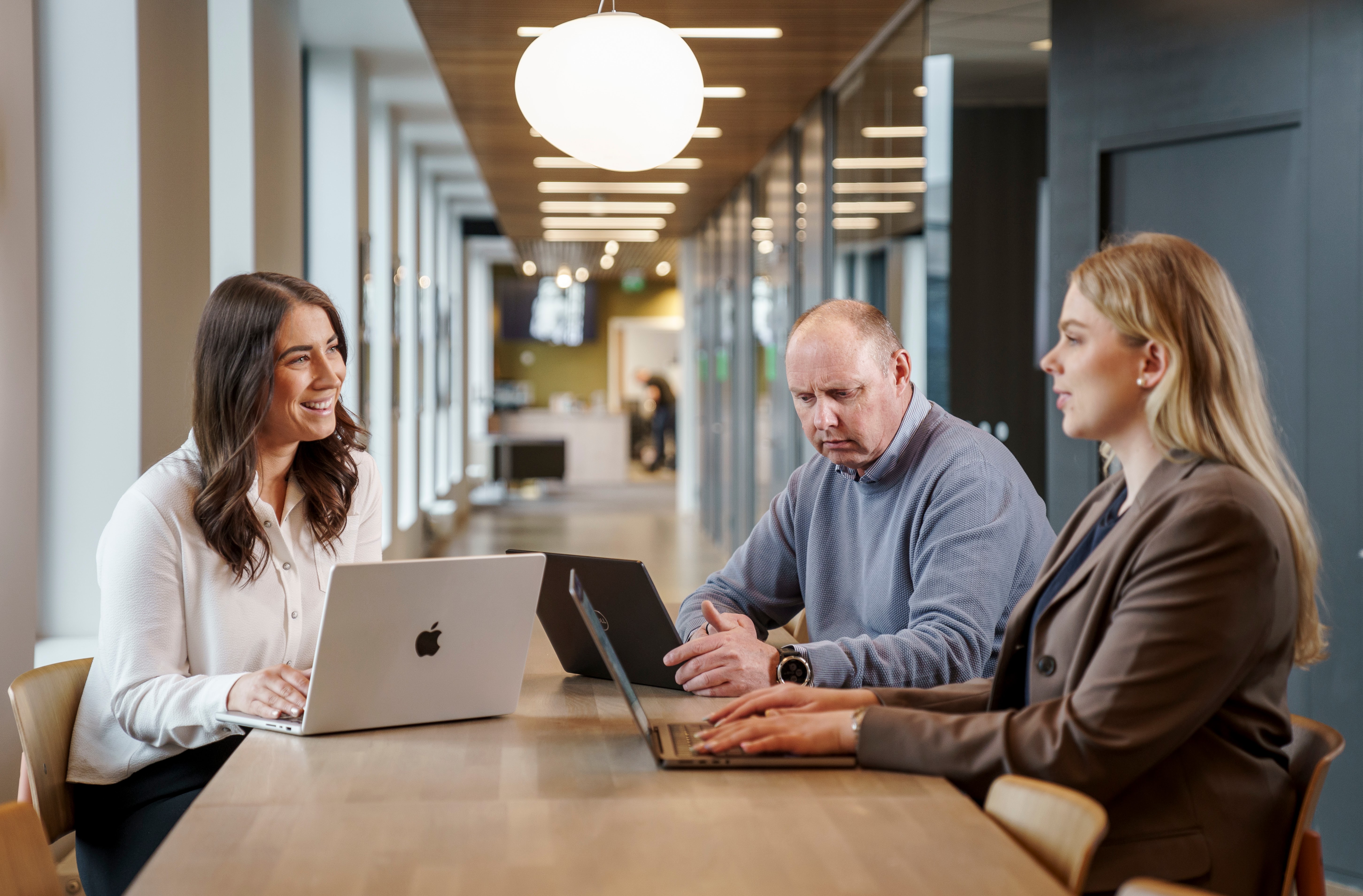 Tre personer som sitter rundt et bord og diskuterer og ser på pc-skjermen 